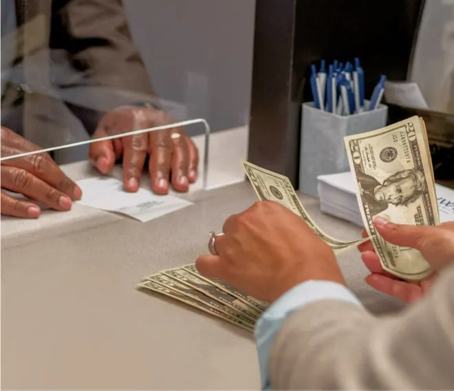 A teller counting bills being behind a bank counter