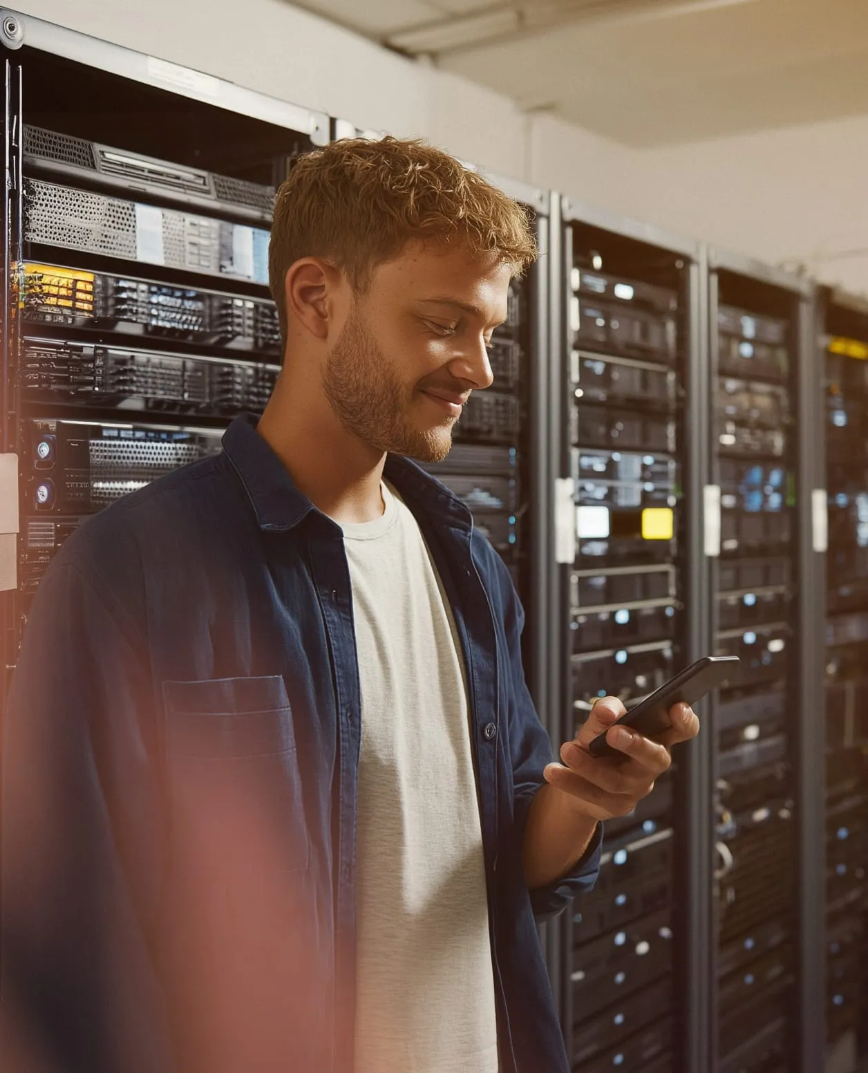 A man checks his mobile phone while standing inside a data center.