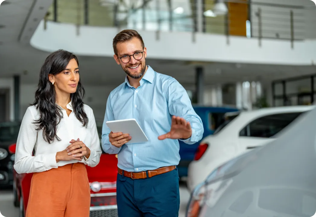 A man and woman examine a tablet while discussing options at a car dealership.