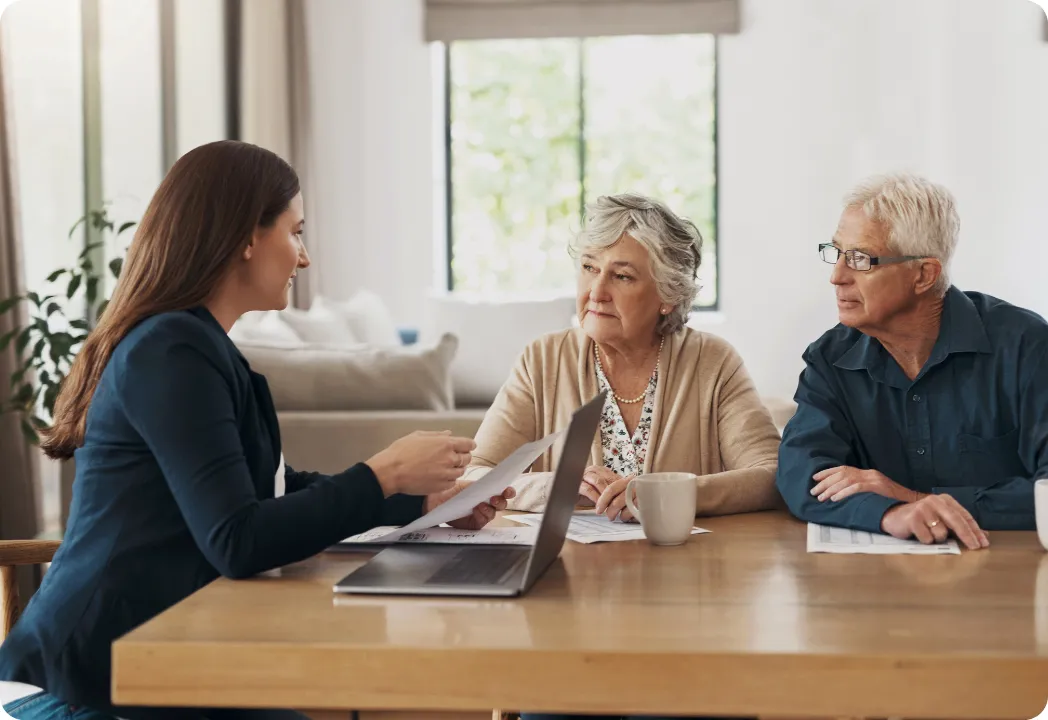 Three individuals, a woman and an old couple, engaged in discussion at a table with a laptop open in front of them.