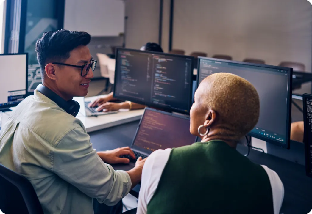 Two individuals focused on their computers while collaborating in a modern office setting.