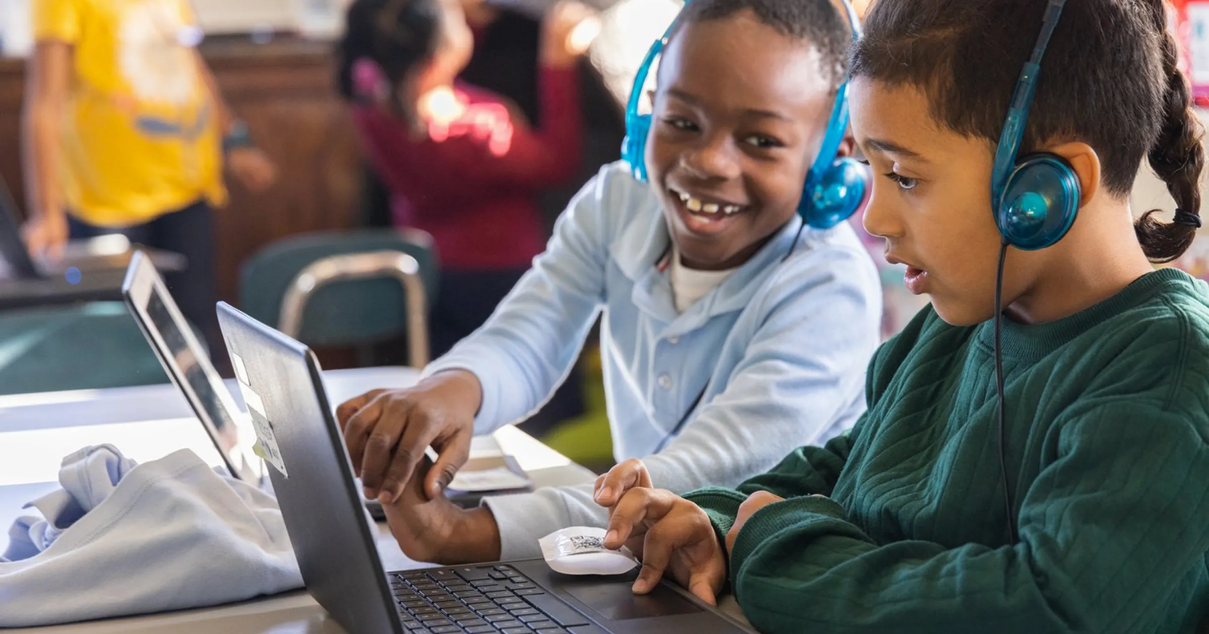 Two kids sitting next to each other and interacting with their laptops