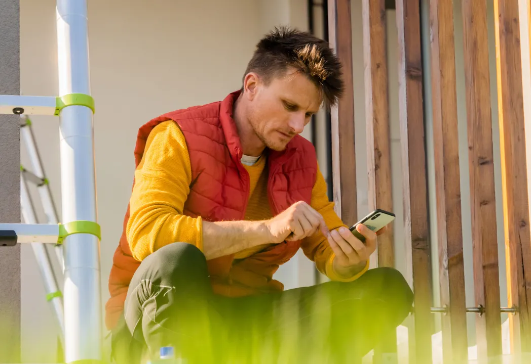 A man sitting on a porch, casually using a cell phone while enjoying the outdoor setting.