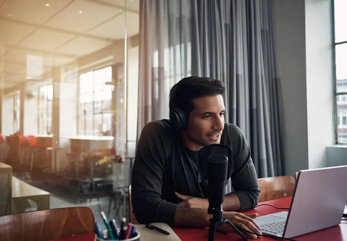 man recording a podcast on a laptop in a modern office